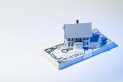 Une petite maison posée sur une liasse de billets